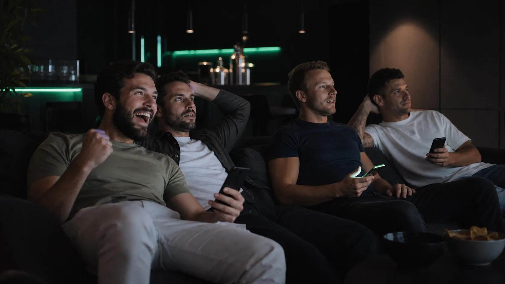 friends on a couch watching a game with glowing phones, dark room